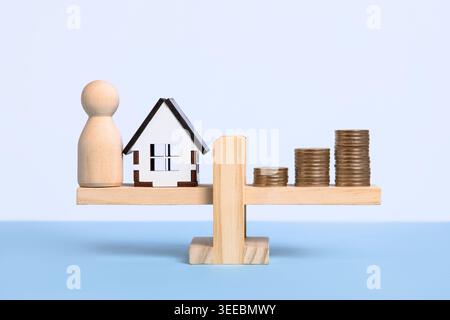 Das Konzept der Balance zwischen Leben und Arbeit wird durch eine hölzerne Waage mit einer menschlichen Figur auf der einen Seite mit einem Haus auf der anderen Seite eines Stapel Münzen dargestellt Stockfoto