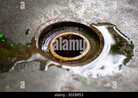 Nahaufnahme eines Abflusslochs für eine Zementspüle mit klarem Wasserpfütze und Lichtreflexion auf einer rauen Oberfläche Stockfoto