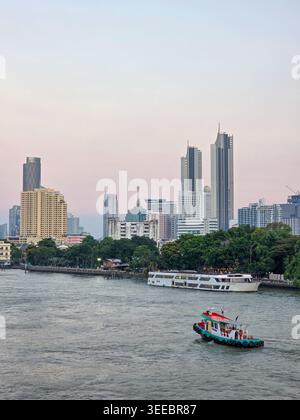 Friedliche Skyline der Stadt, die sich über den breiten Fluss reflektiert, mit einem kleinen Boot, das ruhiges Wasser in der Nähe von städtischen Wolkenkratzern navigiert und das wunderschöne metropoli schafft Stockfoto
