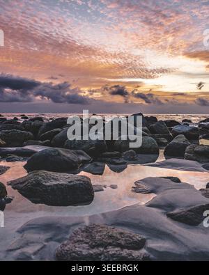 Dramatischer farbenfroher Sonnenuntergang über Vik Beach auf den Lofoten Inseln mit glatten, nassen Felsen, die den goldenen rosa Himmel im flachen Gezeitenwasser in Nordnorwegen reflektieren. Stockfoto