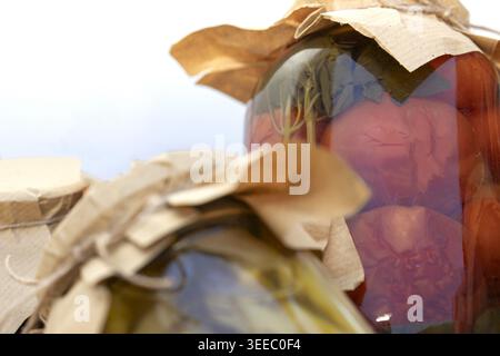 Hausgemachte Dosentomaten im Glasgefäß mit Basilikumblättern-Nahzusammensetzung Stockfoto