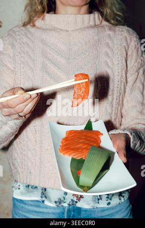 Mädchen isst Lachs-Sashimi mit Stäbchen von einem weißen Teller Stockfoto