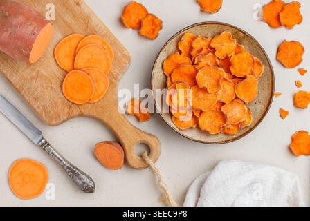 Gesunde Bio-Süßkartoffelchips in einer Schüssel und frische Süßkartoffeln auf einem Holzbrett. Vegetarische und vegane Vorspeise. Diät. Ein nützlicher Snack. Auswahl Stockfoto