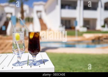 Erfrischende kalte Getränke neben einem ruhigen Resort-Pool mit eleganter Ferienunterkunft und sonniger tropischer Urlaubsatmosphäre in luxuriöser Atmosphäre Stockfoto