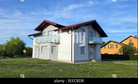 Eine moderne Residenz mit weißer Fassade verfügt über elegante Glasgeländer und eine integrierte Klimaanlage auf einer weitläufigen Kleebläche Stockfoto