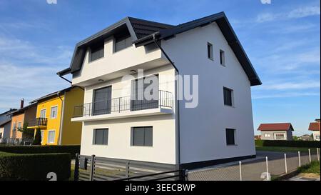 Ein modernes dreistöckiges Familienhaus verfügt über eine frische weiße Fassade, ein dunkelgraues Ziegeldach und passende anthrazitfarbene Fensterläden und Balkongeländer Stockfoto