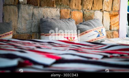 Handgefertigte marokkanische Kissen gegen eine Steinmauer, die Texturen und eine warme, traditionelle Atmosphäre hervorheben. Stockfoto