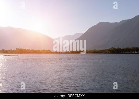 Weite Aussicht auf den See Teletskoje bei Sonnenuntergang mit ruhigem Wasser, bewaldeter Küste und mehrschichtigen Bergsilhouetten in der Republik Altai, Russland, ruhige Natur Stockfoto