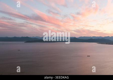Weitläufiger Blick auf die Bucht von Avacha mit ruhigem Wasser, weit entfernten Schiffen und geschichteten Bergsilhouetten unter rosa Sonnenaufgangswolken, in der Nähe von Petropavlovsk-Kamchat Stockfoto