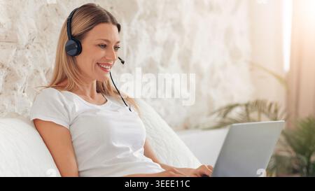Frau mit Headset, die tagsüber am Laptop arbeitet, während sie zu Hause sitzt Stockfoto