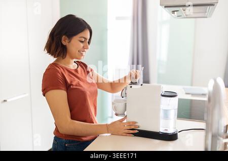 Lächelnde Junge Araberin, Die Kaffee Mit Einer Maschine In Der Küche Zubereitet Stockfoto