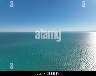 Ein weitläufiger Blick aus der Luft fängt den ruhigen türkisfarbenen Ozean ein, der sich endlos zum Horizont unter einem klaren blauen Himmel mit sanften Wellen erstreckt Stockfoto