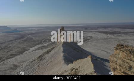 Aus der Vogelperspektive werden hoch aufragende Felsformationen erfasst, die dramatisch aus einer riesigen trockenen Wüstenlandschaft unter einem klaren blauen Himmel mit sanfter Sonne hervorgehen Stockfoto