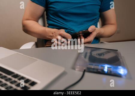 Person wischt die CD mit dem Hemd ab, bevor sie in das externe optische Laufwerk neben dem Laptop eingelegt wird, um Medien für den Datenzugriff, die Sicherung oder die Wiedergabe vorzubereiten Stockfoto