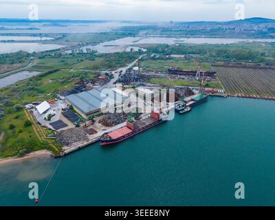 Die Luftaufnahme eines Industriegeländes auf dem Wasser zeigt Schiffe, die an der Werft angedockt sind. Um die Gebäude herum sind Schrotthaufen sichtbar. Stockfoto