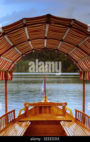 026 farbenfrohe, gestreifte Markise eines modernen Pletna (Holzruderbootes), der am Hafen von Mlino vertäut ist, umrahmt eine herrliche Villa am Nordufer des Bleder Sees. Bled-Slowenien Stockfoto
