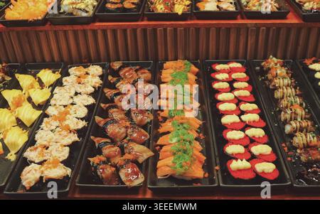 Ansicht verschiedener Sushi-Brötchen auf Markttafeln. Helle Beleuchtung repräsentiert authentische japanische Fusionskultur und asiatische Kleinunternehmen. Stockfoto