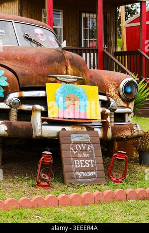 Liebe ist das beste Zutatenschild, das vor einem rostenden Oldtimer angebracht wird, als Hofkunst, die Frieden, Liebe und Mitgefühl in Montgomery Alabama, USA, fördert. Stockfoto