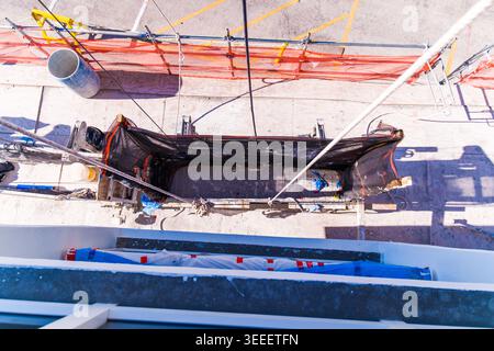 Schwere Seile halten eine abgehängte Holzgerüstplattform mit schwarzem Schutzgitter gegen eine weiße Gebäudeaußenwand. Stockfoto