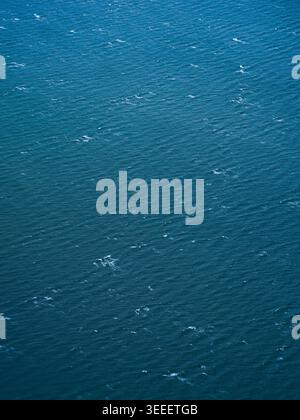 Tiefblaues Meereswasser füllt den Rahmen mit einem sich wiederholenden Muster aus kleinen Wellen und weißen Schaumwänden, die aus einem hohen Blickwinkel aufgenommen wurden. Stockfoto