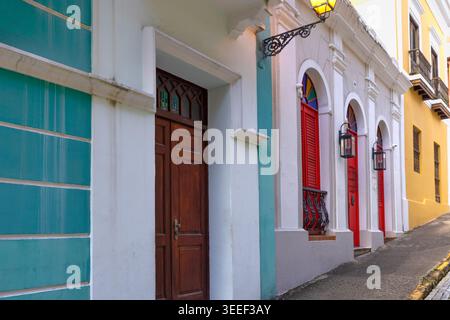 Blick auf eine schräge Kopfsteinpflasterstraße in Old San Juan Puerto Rico mit lebhaften Kolonialgebäuden mit traditionellen Holztüren und geschmiedetem iro Stockfoto
