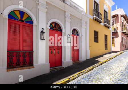Blick auf eine schräge Kopfsteinpflasterstraße in Old San Juan Puerto Rico mit lebhaften Kolonialgebäuden mit traditionellen Holztüren und geschmiedetem iro Stockfoto