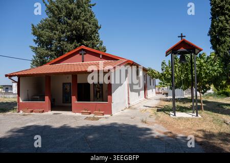 Äußere einer kleinen griechisch-orthodoxen Kapelle mit rotem Ziegeldach, Ikonen und einem Glockenturm unter klarem Himmel in Agia Triada, Griechenland. Stockfoto