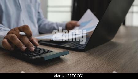 Geschäftsmann, der Rechner mit Finanzdokumenten und Laptop am Bürotisch verwendet, geeignet für Finanzbuchhaltung, Investitionsanalyse, Budgetierung, Stockfoto
