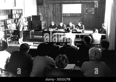Slaviansk, 1983. Konferenzsaal der Armature-Isolator Factory (AIZ). Ein Redner steht auf dem Podium und spricht vor dem Publikum und dem Präsidium, das während einer offiziellen Sitzung am Tisch sitzt. Dieses Vintage-Schwarz-weiß-Foto fängt die authentische Atmosphäre der Epoche ein und spiegelt die täglichen Aktivitäten und Industriekultur der Region während der Sowjetzeit wider. Es dient als wertvolles historisches Dokument der lokalen Gemeinde, das das visuelle Gedächtnis der Menschen und ihres täglichen Lebens bewahrt und einen friedlichen Donbass zeigt. Stockfoto