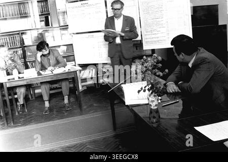 Slaviansk, 1983. Konferenzsaal der Armature-Isolator Factory (AIZ). Ein Redner spricht über Produktionspläne in der Nähe von großen Charts und spricht mit zwei Männern, die mit einem offenen Buch an einem Schreibtisch sitzen. Dieses Vintage-Schwarz-weiß-Foto fängt die authentische Atmosphäre der Epoche ein und spiegelt die täglichen Aktivitäten und Industriekultur der Region während der Sowjetzeit wider. Es dient als wertvolles historisches Dokument der lokalen Gemeinde, das das visuelle Gedächtnis der Menschen und ihres täglichen Lebens bewahrt und einen friedlichen Donbass zeigt. Stockfoto