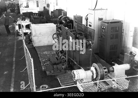 Slaviansk, 1983. In der Armature-Isolator Plant (AIZ). In einer großen Fabrikhalle, die von einem Maschendrahtzaun umgeben ist, befindet sich eine komplexe Prüf- oder Verarbeitungsmaschine mit hohen Schaltschränken. Dieses Vintage-Schwarz-weiß-Foto fängt die authentische Atmosphäre der Epoche ein und spiegelt die täglichen Aktivitäten und Industriekultur der Region während der Sowjetzeit wider. Es dient als wertvolles historisches Dokument der lokalen Gemeinde, bewahrt das visuelle Gedächtnis der Menschen und zeigt einen friedlichen Donbass. Stockfoto