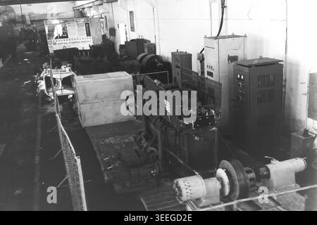 Slaviansk, 1983. In der Armature-Isolator Plant (AIZ). In einer großen Fabrikhalle, die von einem Maschendrahtzaun umgeben ist, befindet sich eine komplexe Prüf- oder Verarbeitungsmaschine mit hohen Schaltschränken. Dieses Vintage-Schwarz-weiß-Foto fängt die authentische Atmosphäre der Epoche ein und spiegelt die täglichen Aktivitäten und Industriekultur der Region während der Sowjetzeit wider. Es dient als wertvolles historisches Dokument der lokalen Gemeinde, bewahrt das visuelle Gedächtnis der Menschen und zeigt einen friedlichen Donbass. Stockfoto
