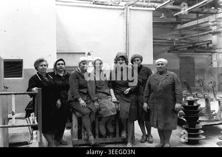 Slaviansk, 1983. In der Armature-Isolator Plant (AIZ). Eine freundliche Gruppe weiblicher Arbeiter sitzt und steht um einen schweren Industriecontainer voller dunkler Keramikisolatoren und lächelt warm für die Kamera. Dieses Vintage-Schwarz-weiß-Foto fängt die authentische Atmosphäre der Epoche ein und spiegelt die täglichen Aktivitäten und Industriekultur der Region während der Sowjetzeit wider. Es dient als wertvolles historisches Dokument der lokalen Gemeinde, bewahrt das visuelle Gedächtnis und zeigt einen friedlichen Donbass. Stockfoto