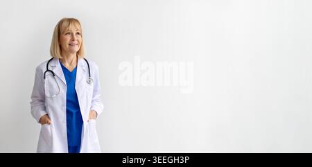 Ärztin in weißem Mantel, die auf weißem Hintergrund mit selbstbewusstem Lächeln steht Stockfoto
