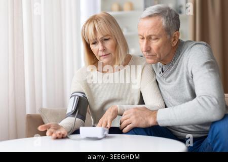 Seniorenpaar, das zu Hause zusammen den Blutdruckmessgerät überprüft Stockfoto