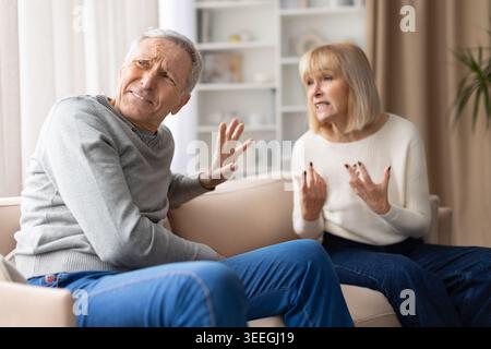 Ein reifes Paar sitzt zu Hause auf dem Sofa und streitet emotional. Beide heben die Hände Stockfoto