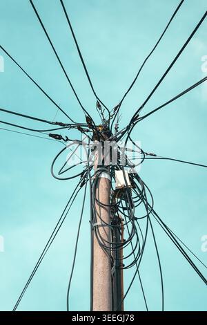 Verworrener Netzmast mit Freileitungen und Kabeln vor klarem blauem Himmel, geringer Blickwinkel Stockfoto
