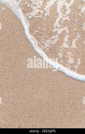 Weißer Meeresschaum von sanften Wellen, die über glattem Sandstrand gespült werden, von oben gesehen. Stockfoto