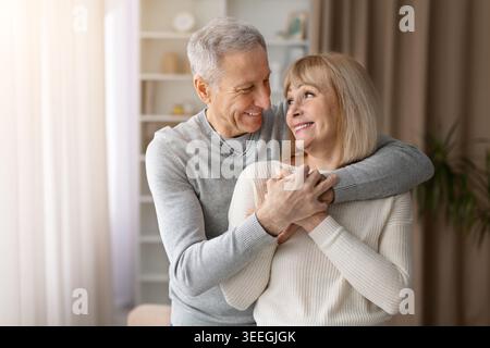 Glückliches, reifes Paar, das sich zu Hause anlächelt und umgibt Stockfoto
