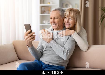 Liebevoll reife Paare, die ihr Smartphone zu Hause nutzen und die Online-Kommunikation genießen Stockfoto