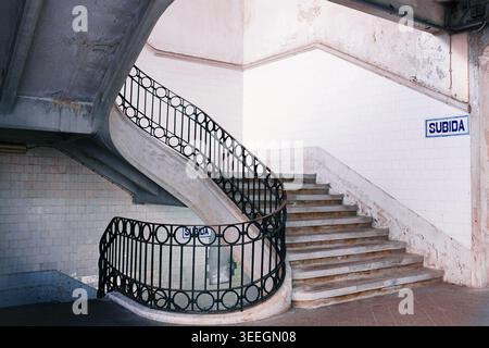 Porto, Portugal: Minimalistische weiße Wendeltreppe mit kunstvoll verzierten schwarzen schmiedeeisernen Geländern und geometrischen Schatten auf dem restaurierten Markt von Bolhão. Stockfoto