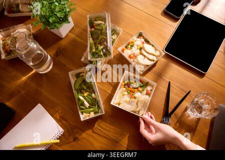 Mittagessen im Büro mit Hühnerreis und Salaten auf hölzernem Besprechungstisch. Stockfoto