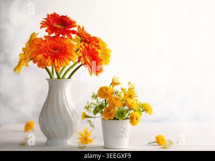 Wunderschöne Blumensträuße aus roten und gelben Blumen in weißen Vasen auf Holztisch, Vorderansicht. Herbststillleben mit Blumen. Stockfoto