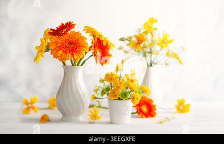 Wunderschöne Blumensträuße aus roten und gelben Blumen in weißen Vasen auf Holztisch, Vorderansicht. Herbststillleben mit Blumen. Stockfoto