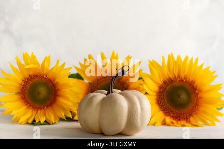 Herbststillleben mit Sonnenblumen und weißem Kürbis. Herbstarrangement auf einem weißen Holztisch. Stockfoto