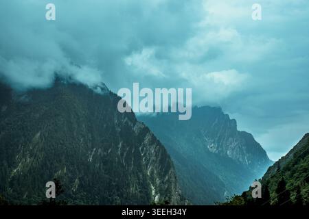 Dramatische Berglandschaft mit dichten grünen Wäldern an steilen Hängen, teilweise verdeckt von atmosphärischem Nebel und Wolken. tal der Blumen, Uttarakhan Stockfoto