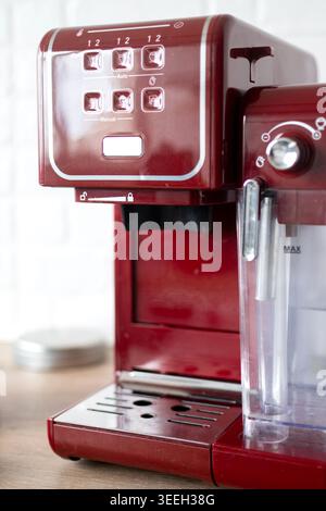 Vertikale Nahaufnahme einer roten Espressomaschine auf einer Küchenarbeitsplatte mit weichem Tageslicht und geringer Schärfentiefe. Moderner Kaffee Stockfoto