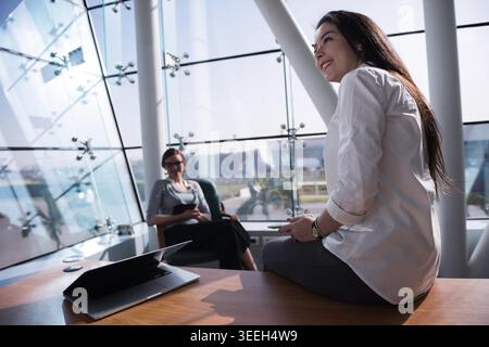 Geschäftskollegen sitzen und unterhalten sich in einem modernen, lichtdurchfluteten Open-Office mit Laptops und Smartphones, während sie während eines zwanglosen Meetings zusammenarbeiten, Brainstorming sammeln und professionelle Kontakte aufbauen. Stockfoto