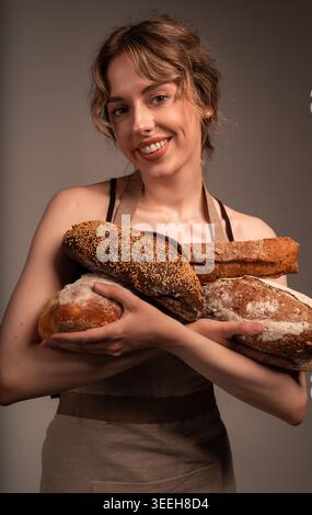 Lächelnde Bäckerin, die frisch gebackenes Brot, Brote und Baguettes hält und gesundes hausgemachtes Essen genießt Stockfoto