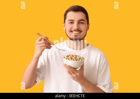 Schöner junger Mann, der leckere Müsliringe auf gelbem Hintergrund isst Stockfoto